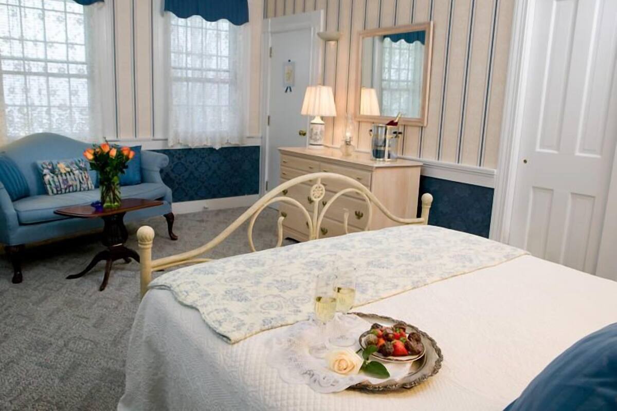A bedroom with a bed, a dresser, a vanity with a mirror, a blue armchair, and a small table with a vase of flowers.