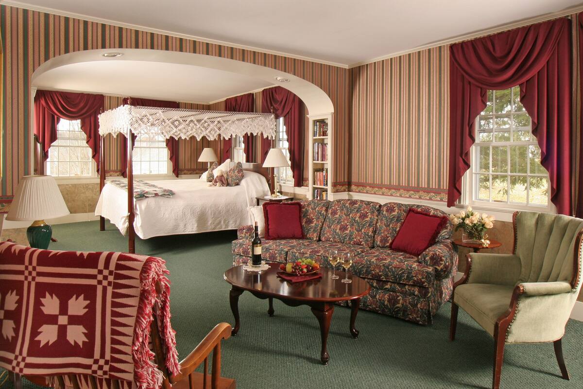 A bedroom with a four-poster bed, a sofa, a chair, and a coffee table.
