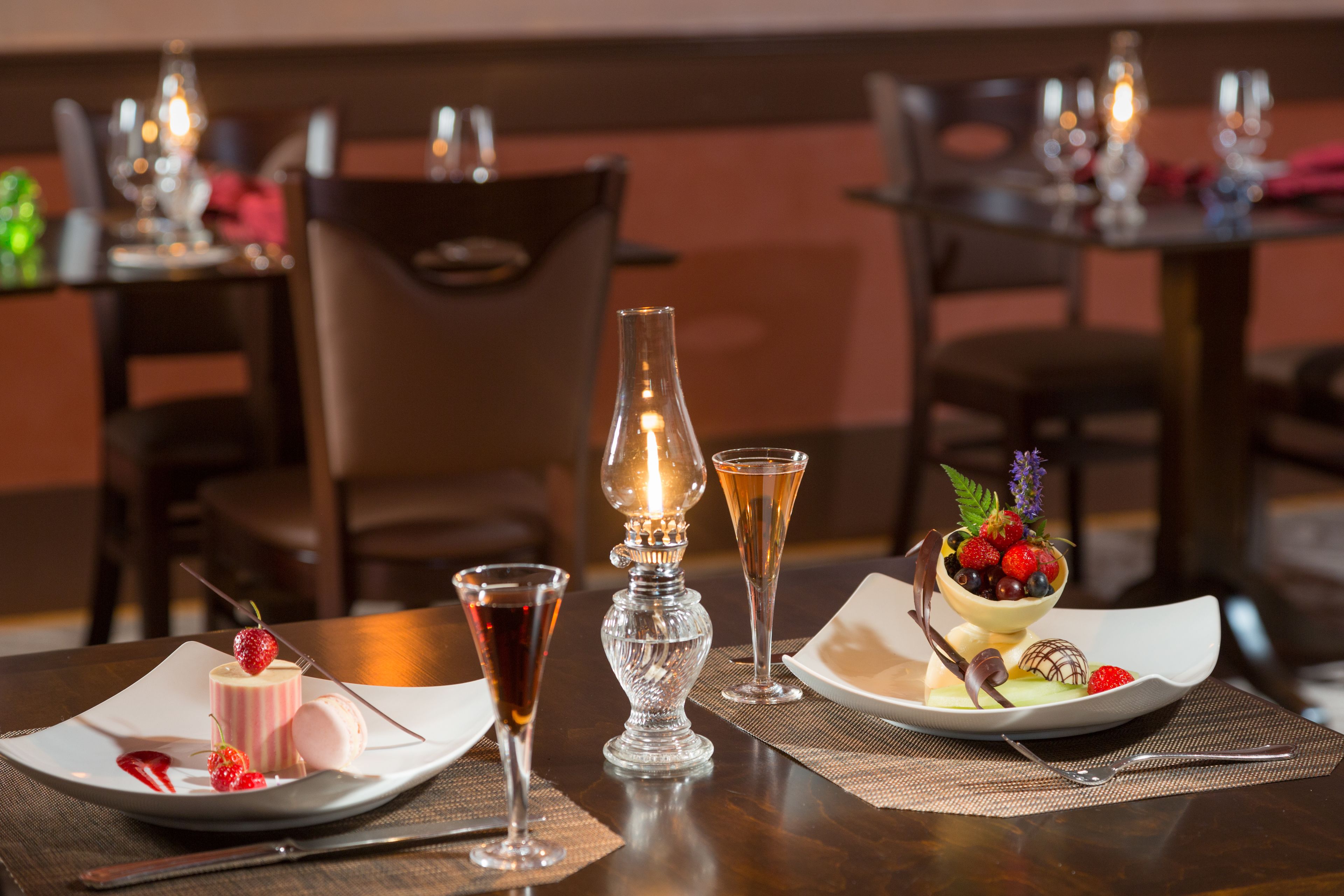 A dining table set with a dessert plate, two glasses, a candle, and a macaron.