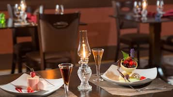 Une table dressée pour le dîner, avec une assiette à dessert, deux verres, une bougie et un macaron.