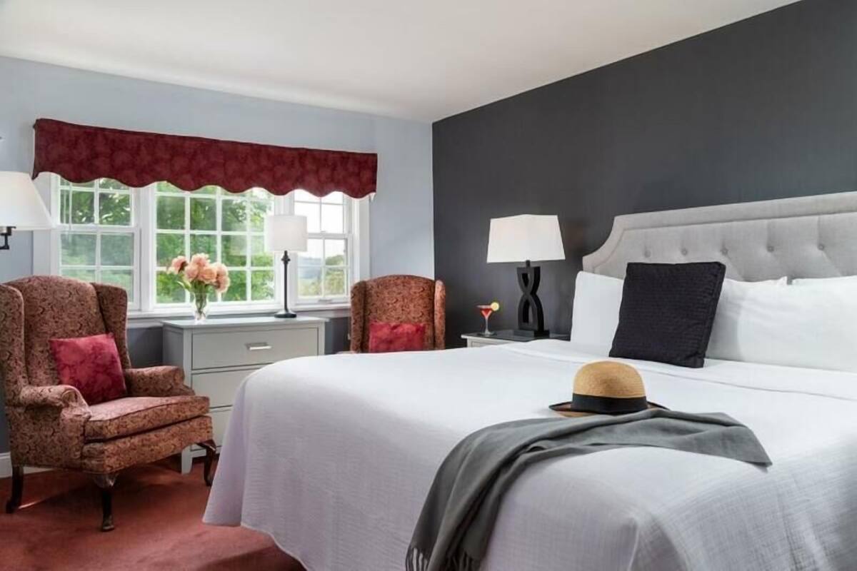 A bedroom with a large bed, two bedside tables, a chair, and a window with curtains.