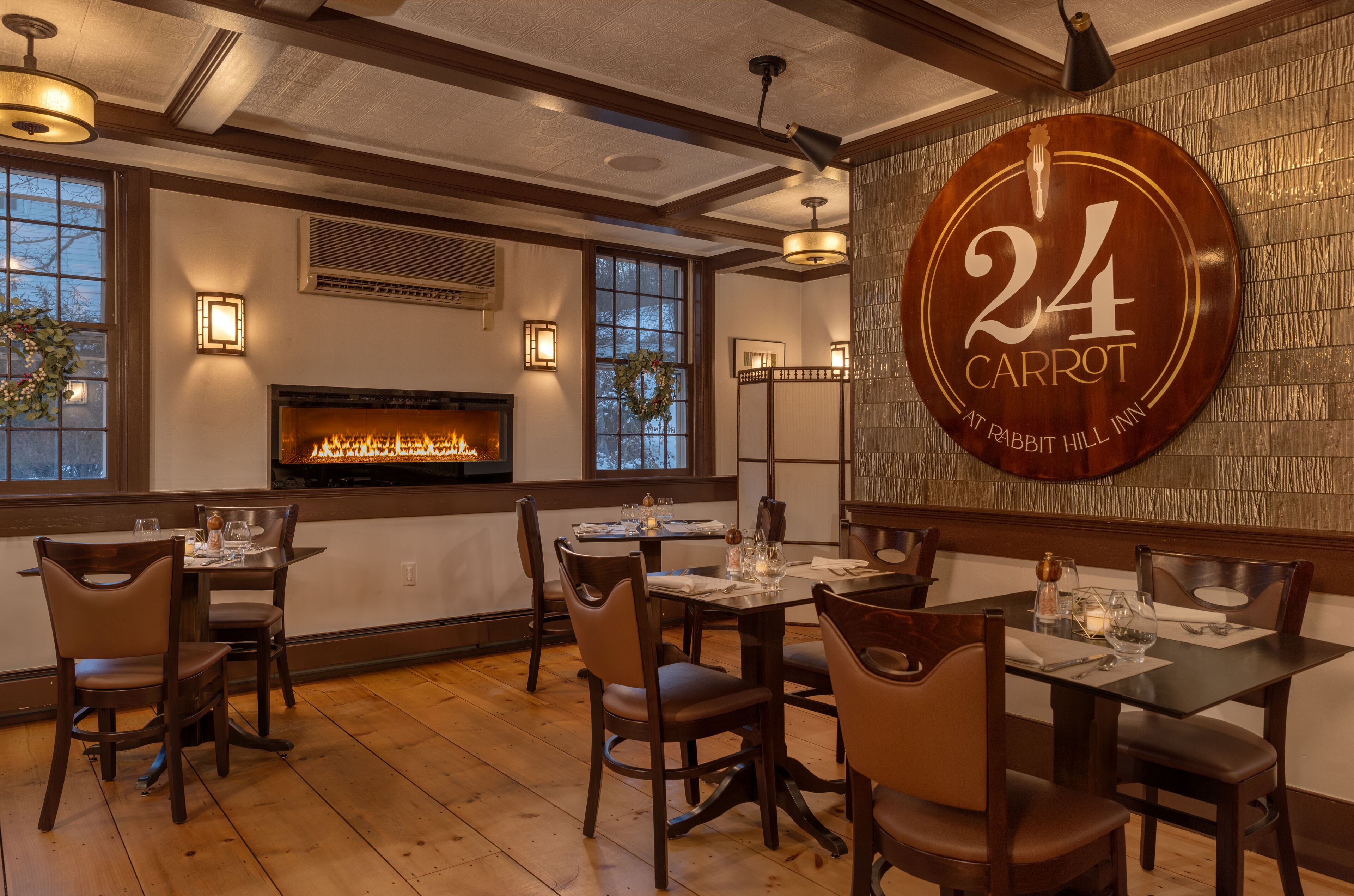 A restaurant interior with a fireplace, wooden flooring, and a wall sign reading "24 CARROT AT RABBIT HILL INN".
