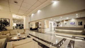 A modern hotel lobby with a reception desk, seating area, and a large plant.