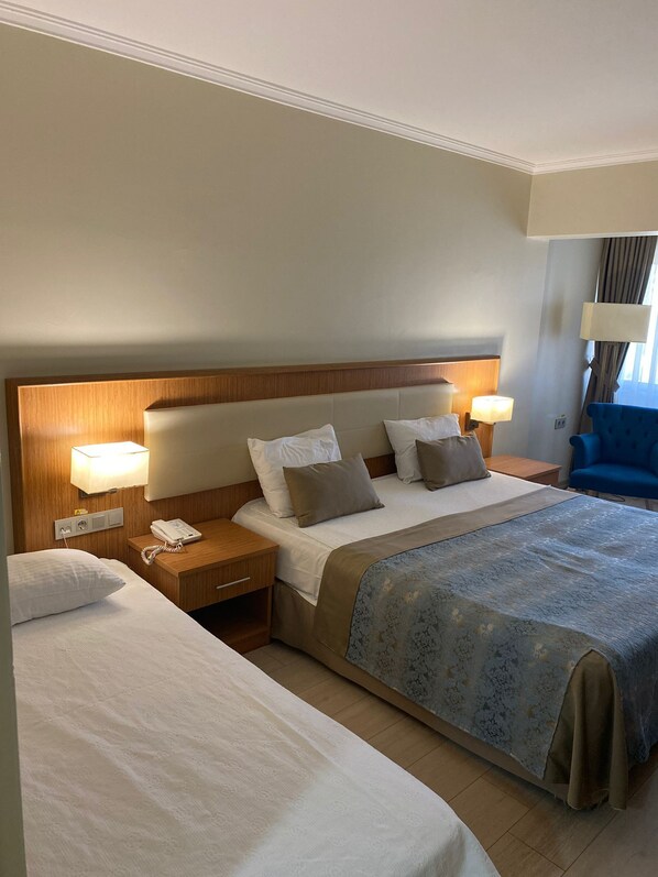A hotel room with a large bed, a smaller bed, a wooden headboard, bedside lamps, a telephone, and a blue chair.