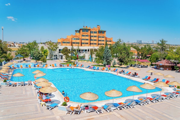 Una piscina grande rodeada de sillas de descanso y sombrillas, con un edificio de hotel al fondo.