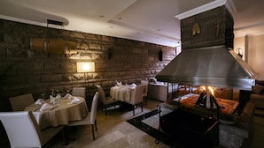 A restaurant with stone walls, a large fireplace, and tables set for dining.