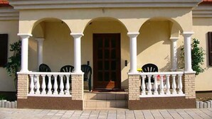 A building with a red-tiled roof, a beige facade, and a covered porch with white balustrades.