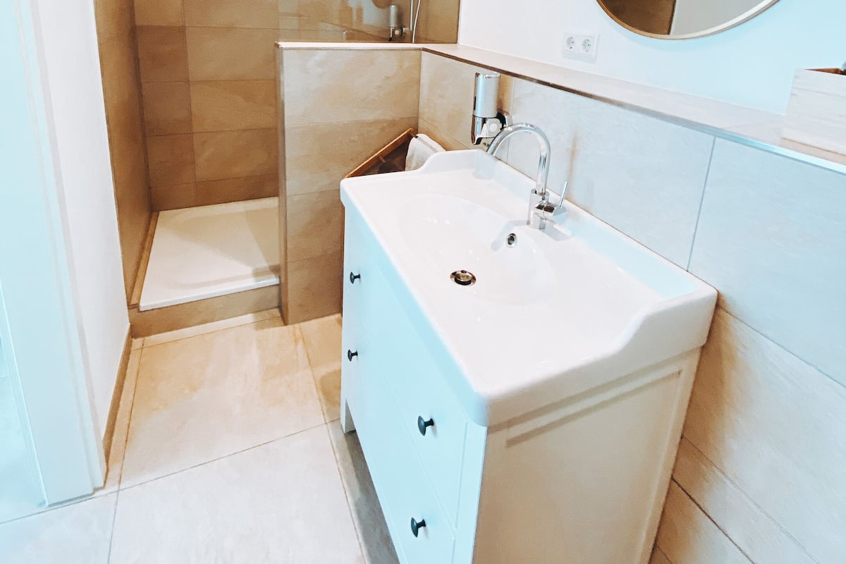 A modern bathroom with a walk-in shower, a large mirror, and a white sink with a cabinet.
