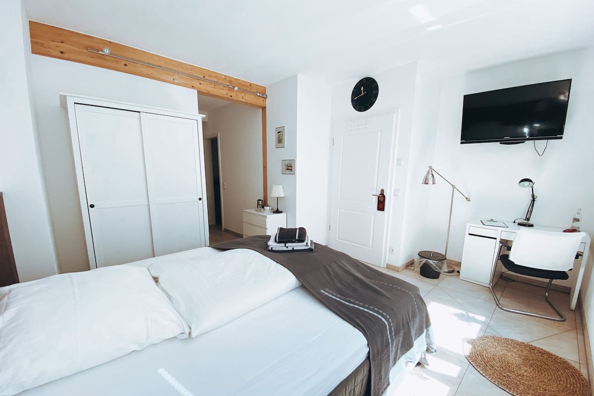 A hotel room with a bed, desk, TV, and a door leading to another room.