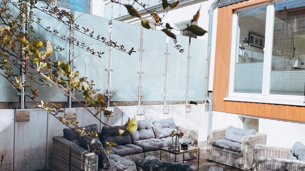Un área de estar exterior moderna con mobiliario de mimbre y una pared de cristal.