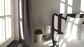 A bedroom with a bed, a nightstand, a lamp, a potted plant, and a window with curtains.