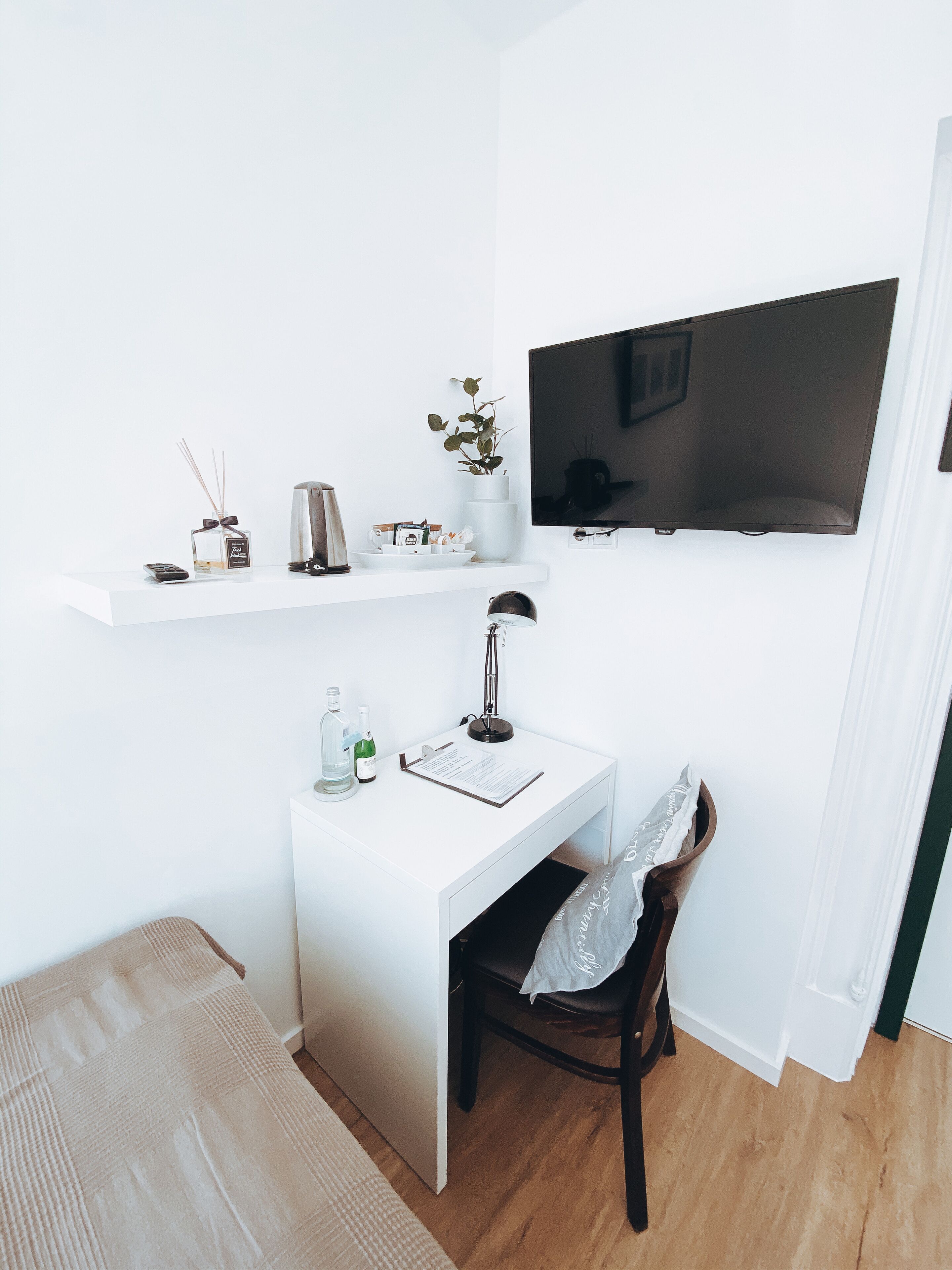Una habitación pequeña y blanca con un escritorio, una silla y un televisor montado.
