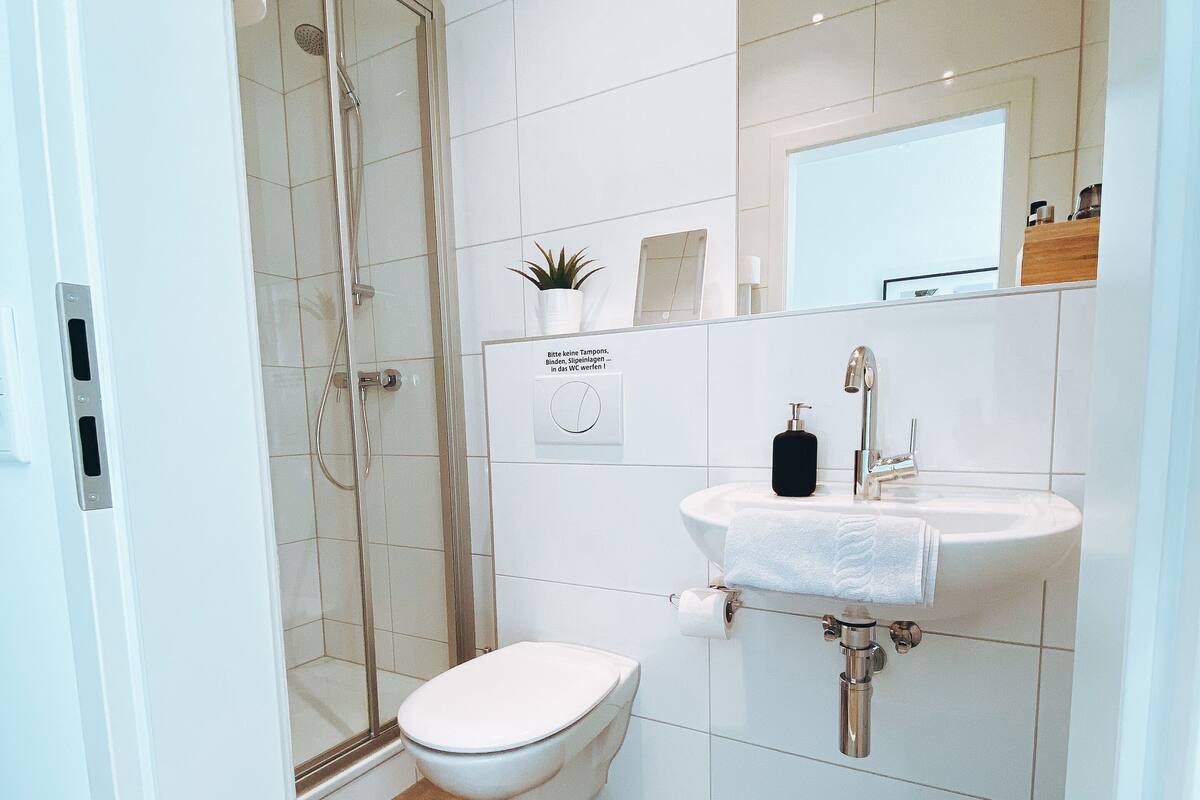 A modern bathroom with a glass-enclosed shower, a white toilet, and a sink with a mirror above it.