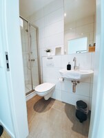 Un baño moderno con ducha envuelta en vidrio, inodoro blanco y lavamanos con espejo arriba.