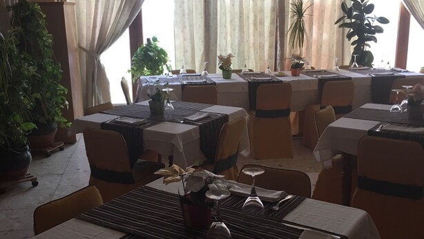 A restaurant with multiple tables set for dining, each with a white tablecloth and a centerpiece of flowers. - Hostal Castilla (Torrenueva)