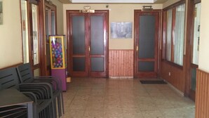 A hallway with a tiled floor, wooden doors, and a row of black chairs on one side. - Hostal Castilla (Torrenueva)