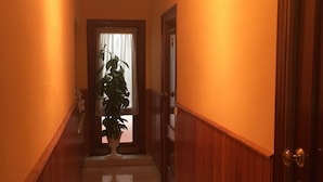 A hallway with wooden paneling, a potted plant, and a door at the end. - Hostal Castilla (Torrenueva)