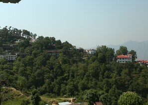 A hillside residential area with multiple houses, dense greenery, and distant mountains. - Hotel Devlok Primal (Dehradun)