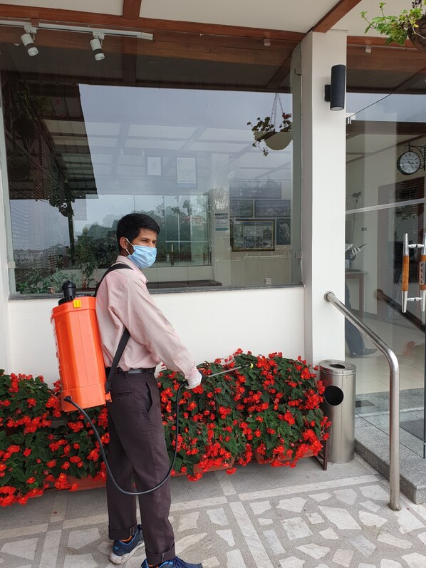 A person with a backpack spraying plants near a building entrance.