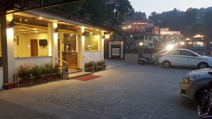 Entrada de hotel con mostrador de recepción, una escalera y plantas en macetas.