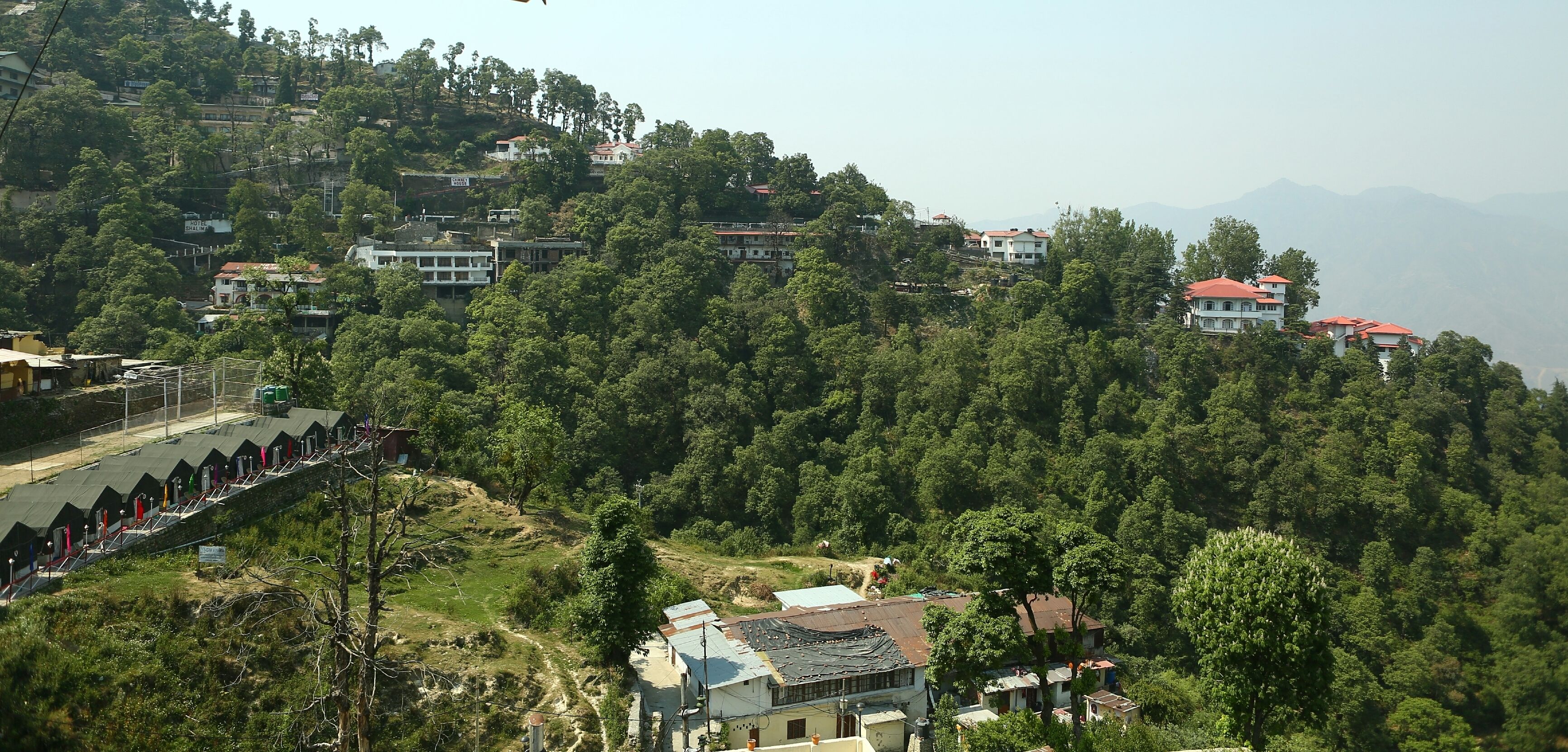 Un pueblo en la ladera de una colina con casas construidas en terrazas, rodeado de un bosque denso.