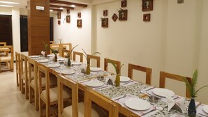 Un comedor con una mesa larga dispuesta para varias personas, sillas de madera y decoración en la pared.