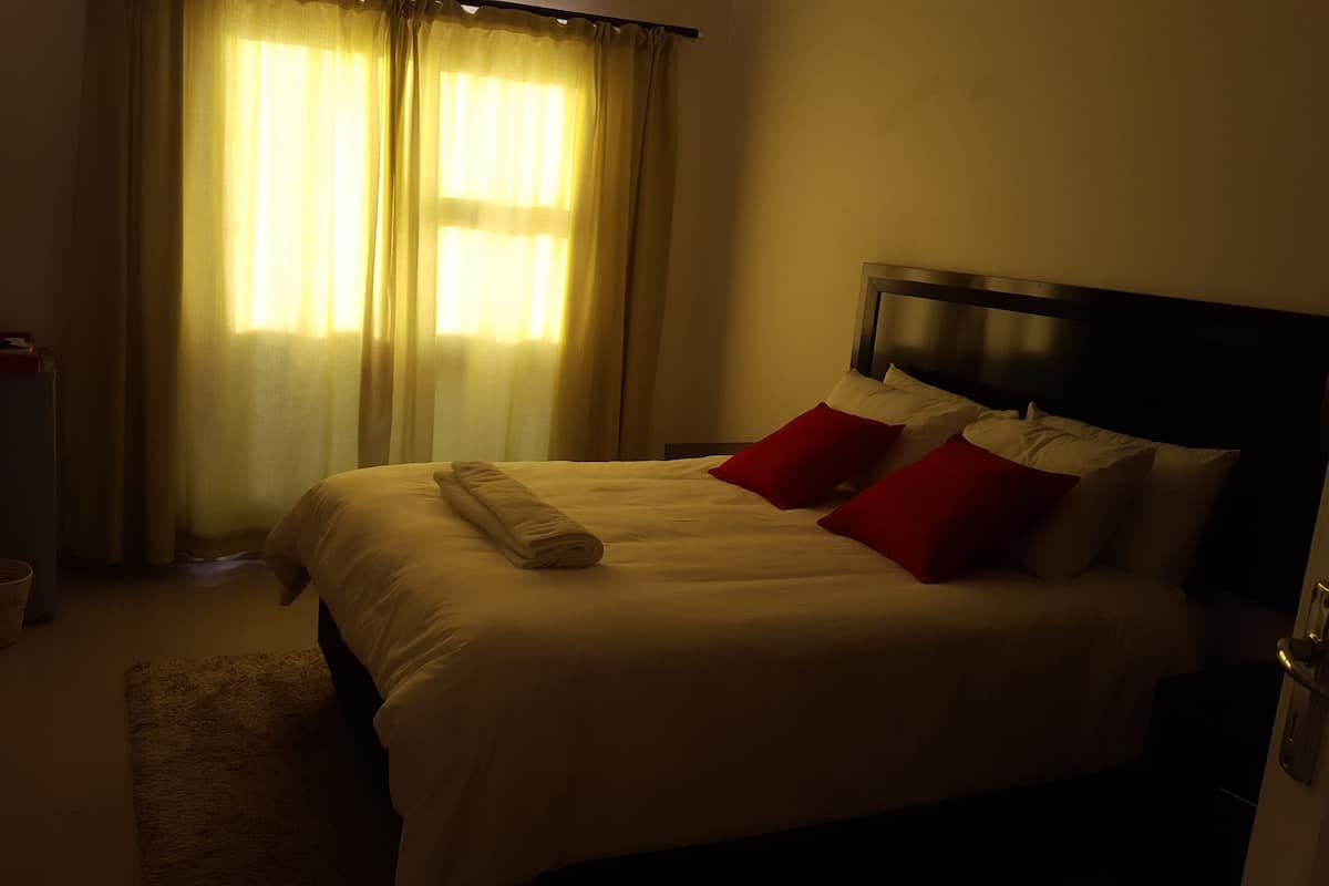 A hotel room with a bed, a nightstand, a lamp, and a window with curtains.