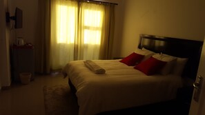 A hotel room with a bed, a nightstand, a lamp, and a window with curtains. - Styled Bed and Breakfast (Palapye)