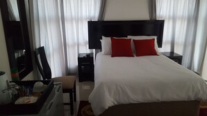 A hotel room with a large bed, a bedside table, a nightstand, a chair, a desk, and a mirror. - Styled Bed and Breakfast (Palapye)