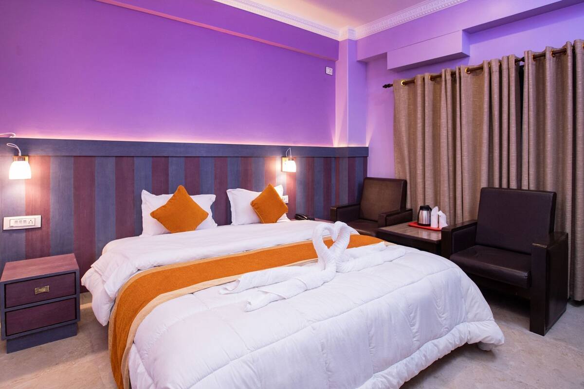 Une chambre d’hôtel avec un lit, des tables de chevet, une chaise et un rideau.