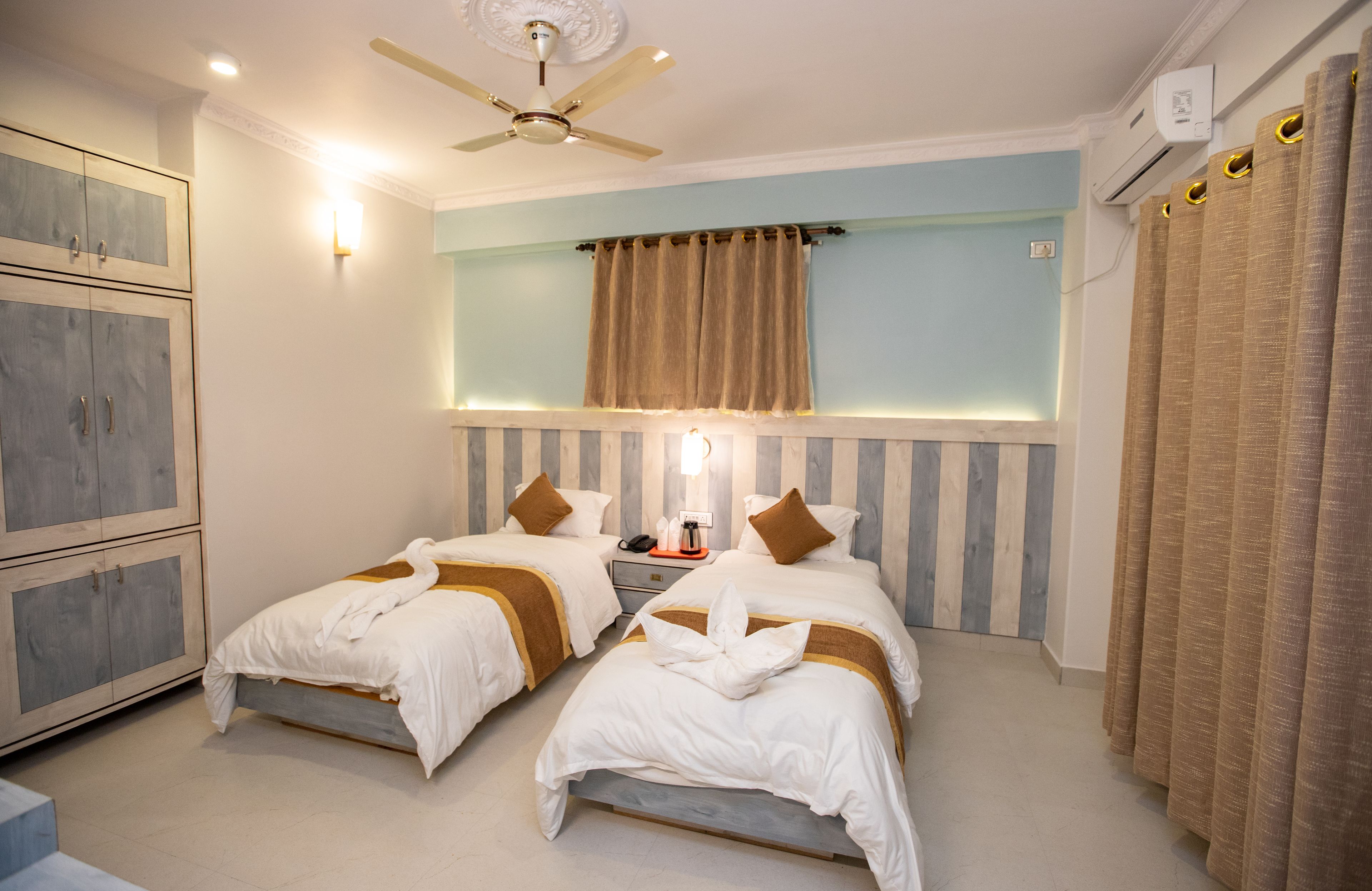 Une chambre d’hôtel avec deux lits, un ventilateur de plafond, une table de chevet avec un téléphone et un climatiseur fixé au mur.