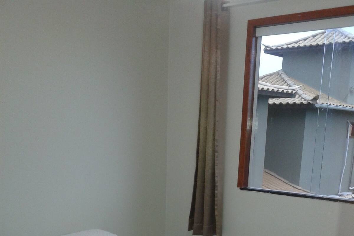 A small, simple room with a bed, a window, and a curtain.