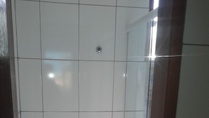A small bathroom with a toilet, a trash bin, and a glass shower enclosure. - Buzios Apartamentos (Búzios)