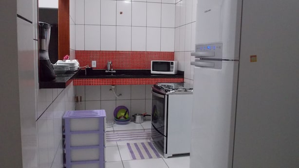 A compact kitchen with white cabinets, a red backsplash, a microwave, a stove, and a refrigerator. - Buzios Apartamentos (Búzios)
