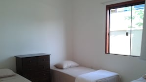 A small, clean room with two single beds, a dresser, and a window providing natural light. - Buzios Apartamentos (Búzios)