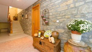 A stone-walled hallway with a wooden staircase, a wooden chest, and a potted plant. - Casa Puyuelo (La Fueva)
