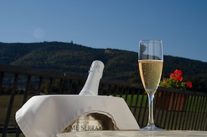 Une bouteille de vin et un verre de vin sont posés sur une table, avec en arrière-plan un paysage pittoresque de collines et de fleurs.