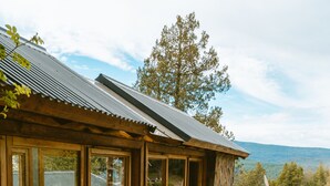A log cabin with large windows and a stone foundation, surrounded by blooming flowers and trees. - Arrayan Lake View Mountain Lodge & Casa De Te Arrayan (San Martín de los Andes)