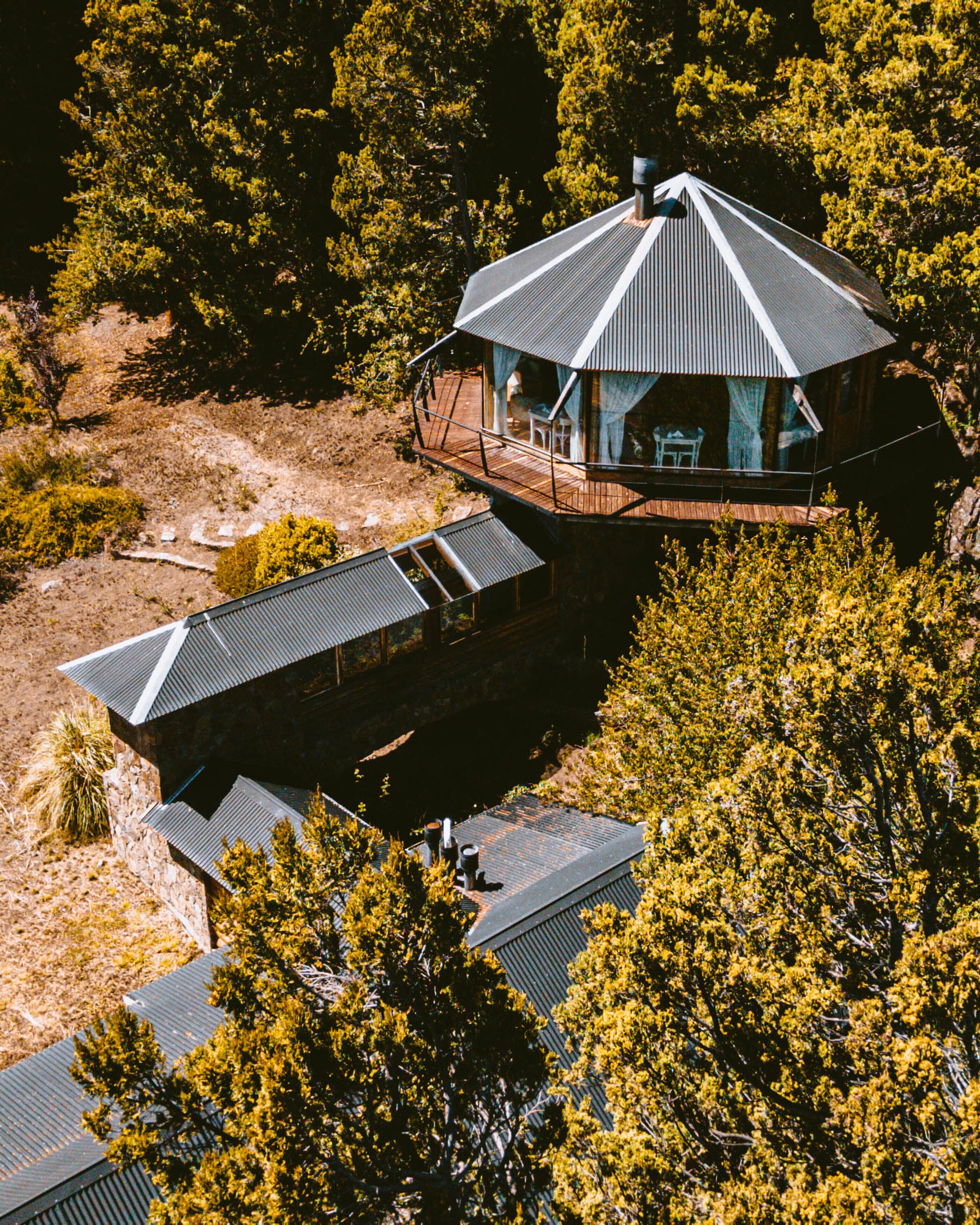 Une maison moderne dotée d’une grande terrasse et de plusieurs toits, entourée d’une forêt dense.
