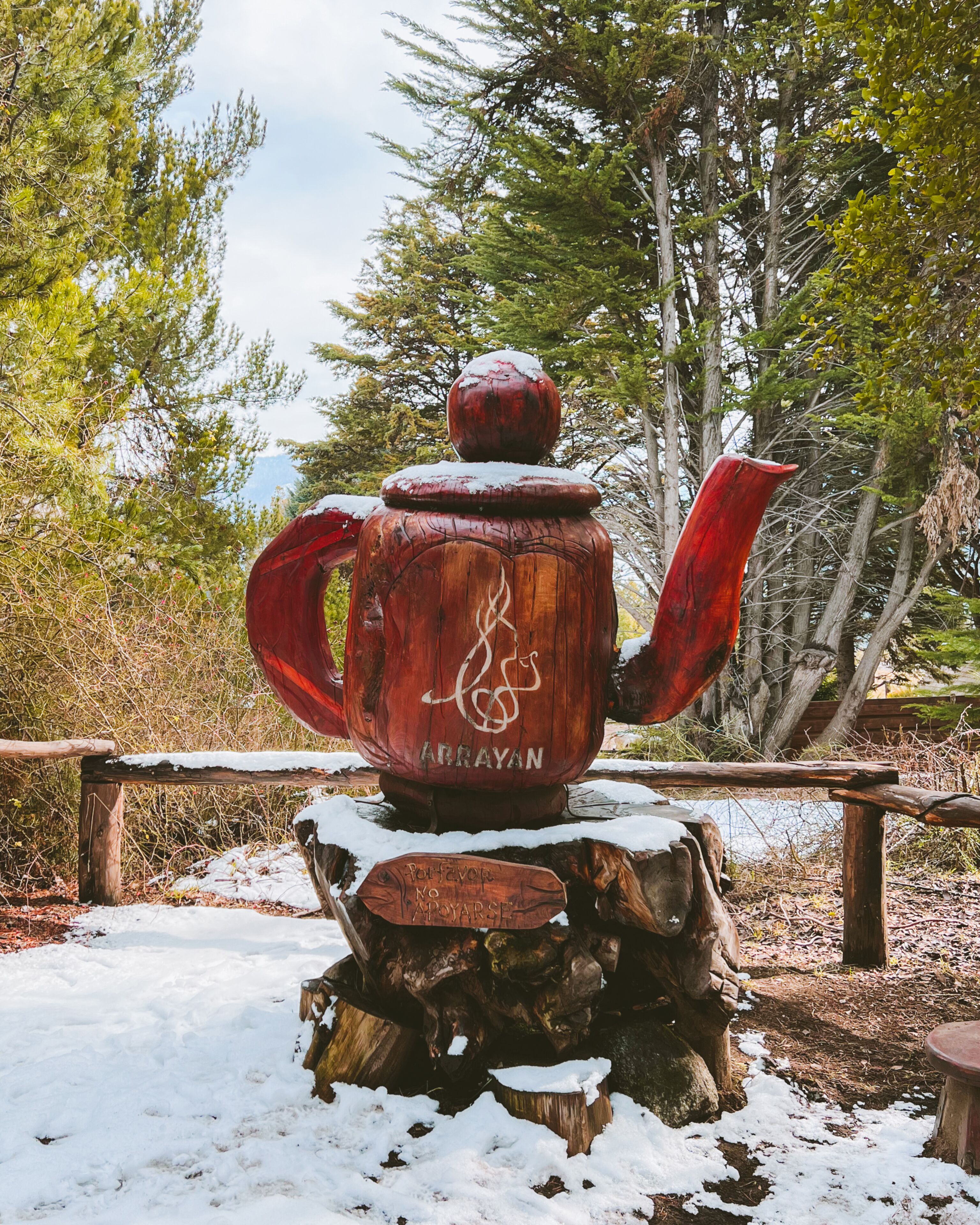 A wooden teapot with a logo on a wooden stump in a snowy outdoor setting.