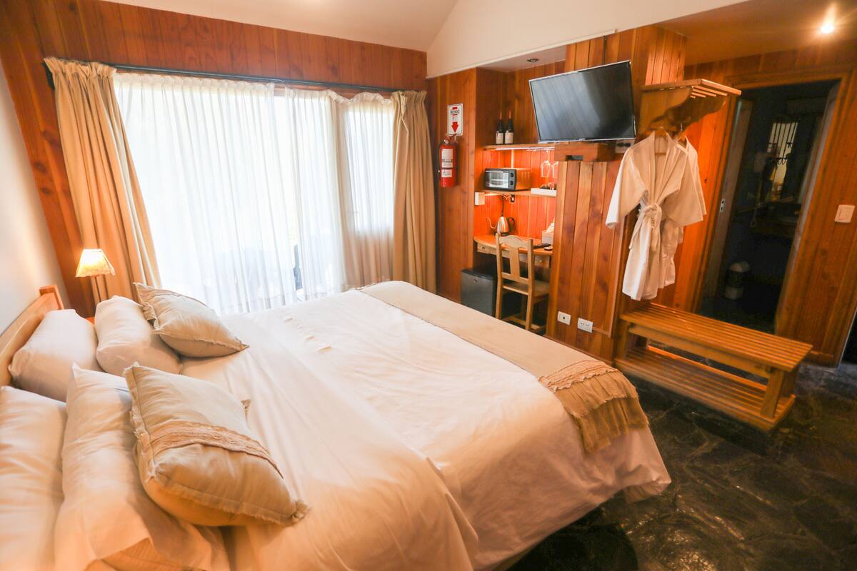 Ein Hotelzimmer mit einem großen Bett, einem Schreibtisch mit Stuhl, einem an der Wand befestigten Fernseher und einem Bademantel an einem Kleiderständer.