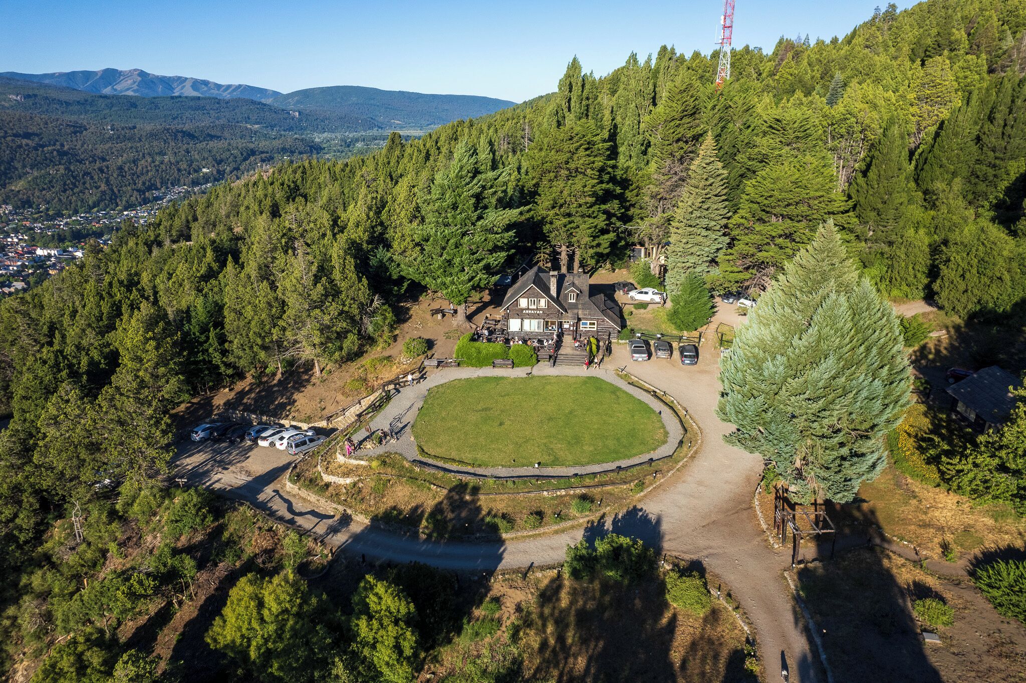 A lodge with a large lawn, surrounded by dense forest and mountains in the background.