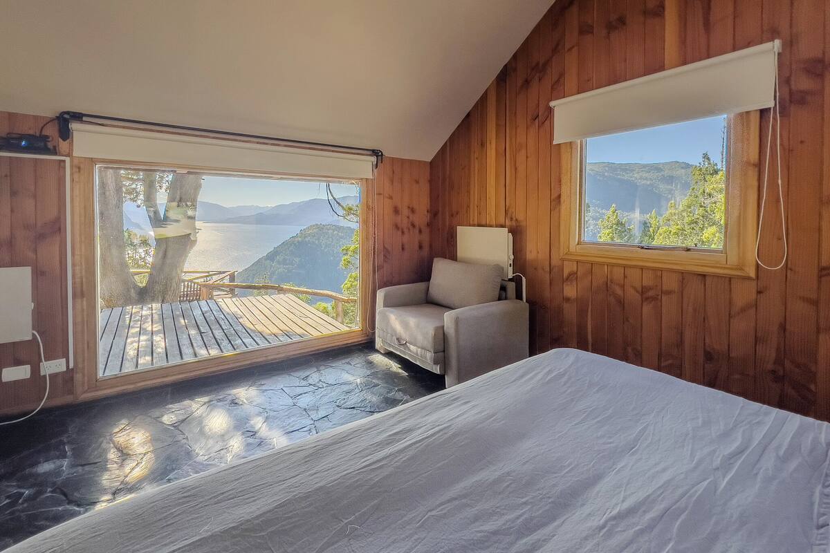 Ein Zimmer mit Bett, Stuhl und Blick auf einen See und Berge.