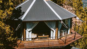 Una cabaña con terraza de madera, chimenea y un ventanal grande.