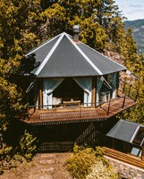 A cabin with a wooden deck, a chimney, and a large window.