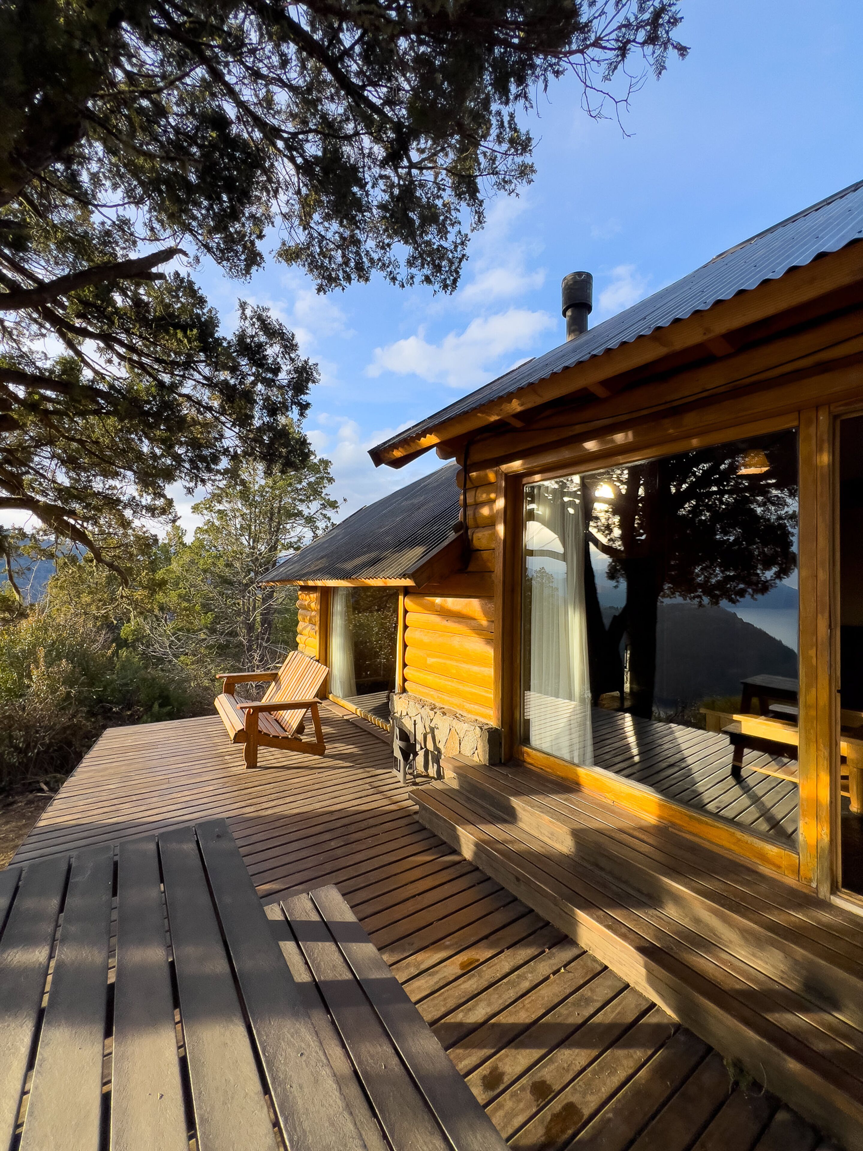 Una baita di legno con una veranda, una panchina e vista sulla foresta e sulle montagne circostanti.