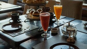 A dining table set with a tiered pastry stand, a glass of orange juice, and a teapot. - Arrayan Lake View Mountain Lodge & Casa De Te Arrayan (San Martín de los Andes)