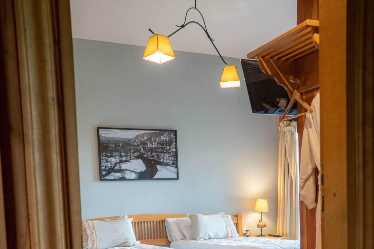 Ein Schlafzimmer mit zwei Betten, einer hölzernen Bank, einem Gemälde an der Wand und einer Deckenleuchte.