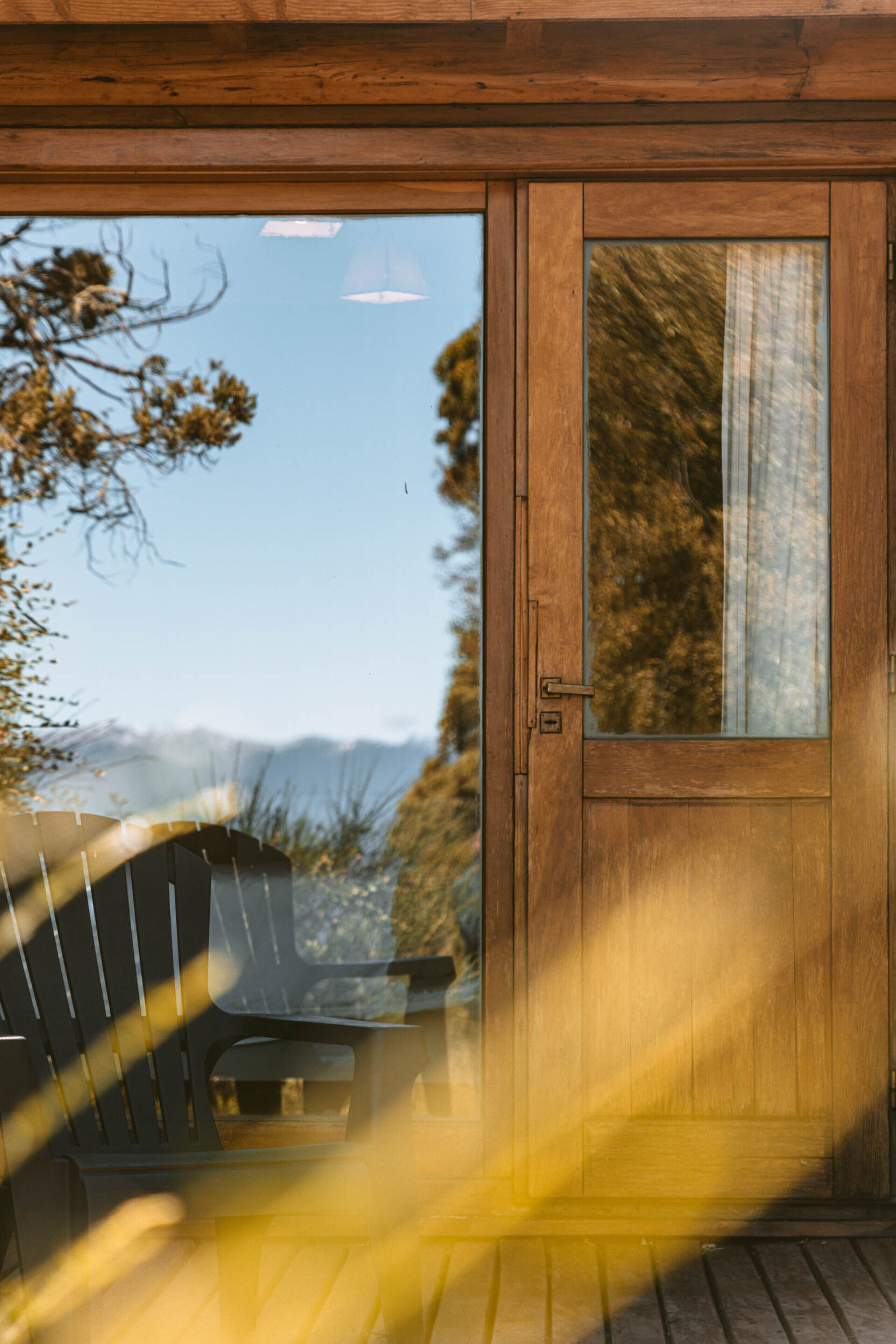 Una puerta de madera con un panel de vidrio, una terraza de madera y vistas a árboles y montañas.