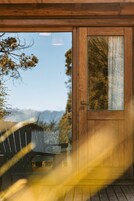 Una puerta de madera con un panel de vidrio, una terraza de madera y vistas a árboles y montañas.